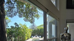 A modern room with large windows overlooking a well-maintained garden and a clear blue sky. - Lands Fine Art Gallery  (Hollywood)