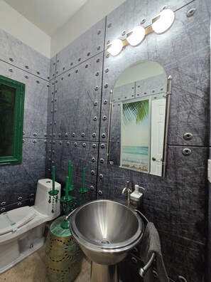 A bathroom with a large sink, a toilet, a mirror, and a wall-mounted light fixture.