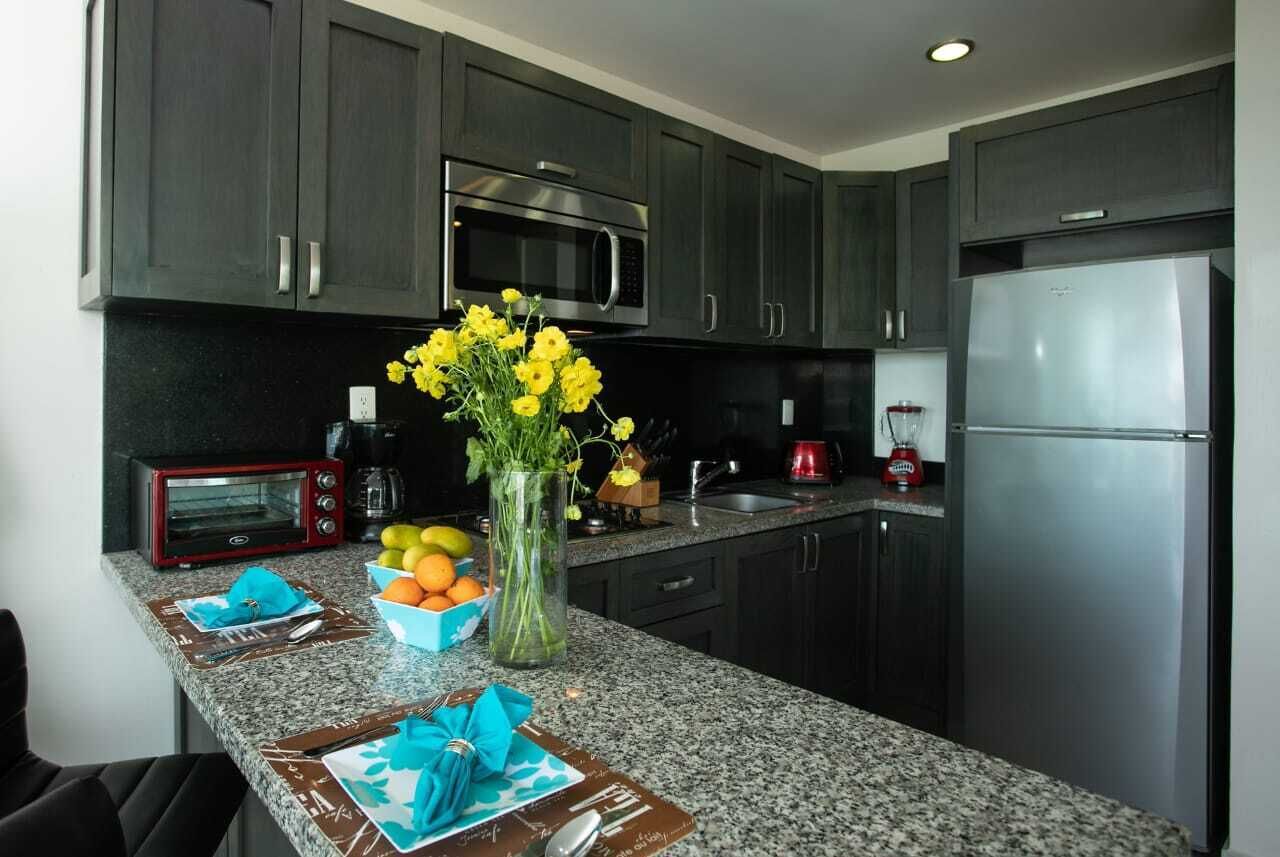 A kitchen with dark cabinets, a stainless steel refrigerator, a microwave, a toaster, and a vase with yellow flowers.