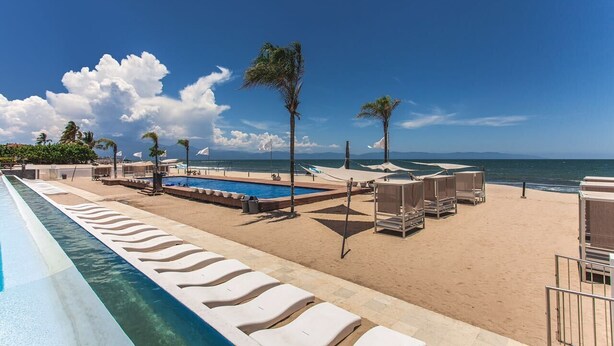 Ein Poolbereich mit Liegestühlen, einem Pool und Blick auf den Strand.