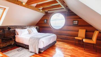A bedroom with a wooden ceiling, a large round window, a bed, a chair, and a dresser.
