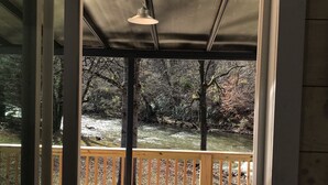 Una terraza techada al aire libre con una mesa y sillas, con vista a un río y zona boscosa.