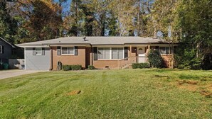 A single-story house with a brick facade, a front porch, and a well-maintained lawn. - Stylish Stone Mountain home, sleeps 8 (Stone Mountain)
