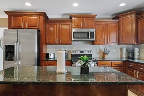 Una cocina con gabinetes de madera, electrodomésticos de acero inoxidable, encimeras de granito y una isla central con una planta.