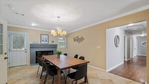 A dining area with a wooden table, black chairs, a chandelier, a fireplace, and a door leading to another room. - Stylish Stone Mountain home, sleeps 8 (Stone Mountain)