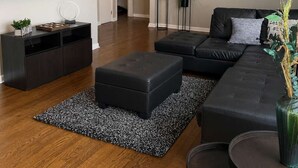 A modern living room with a flat-screen TV, a ceiling fan, a black leather sofa, and a coffee table. - Stylish Stone Mountain home, sleeps 8 (Stone Mountain)