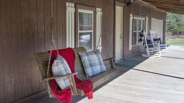 A wooden porch with a swing chair and a bench, both with cushions. - Rustic Countryside Cottage (Cleveland)