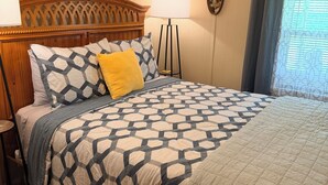 A bedroom with a wooden headboard, a patterned bedspread, a bedside lamp, and a window with curtains. - Rustic Countryside Cottage (Cleveland)