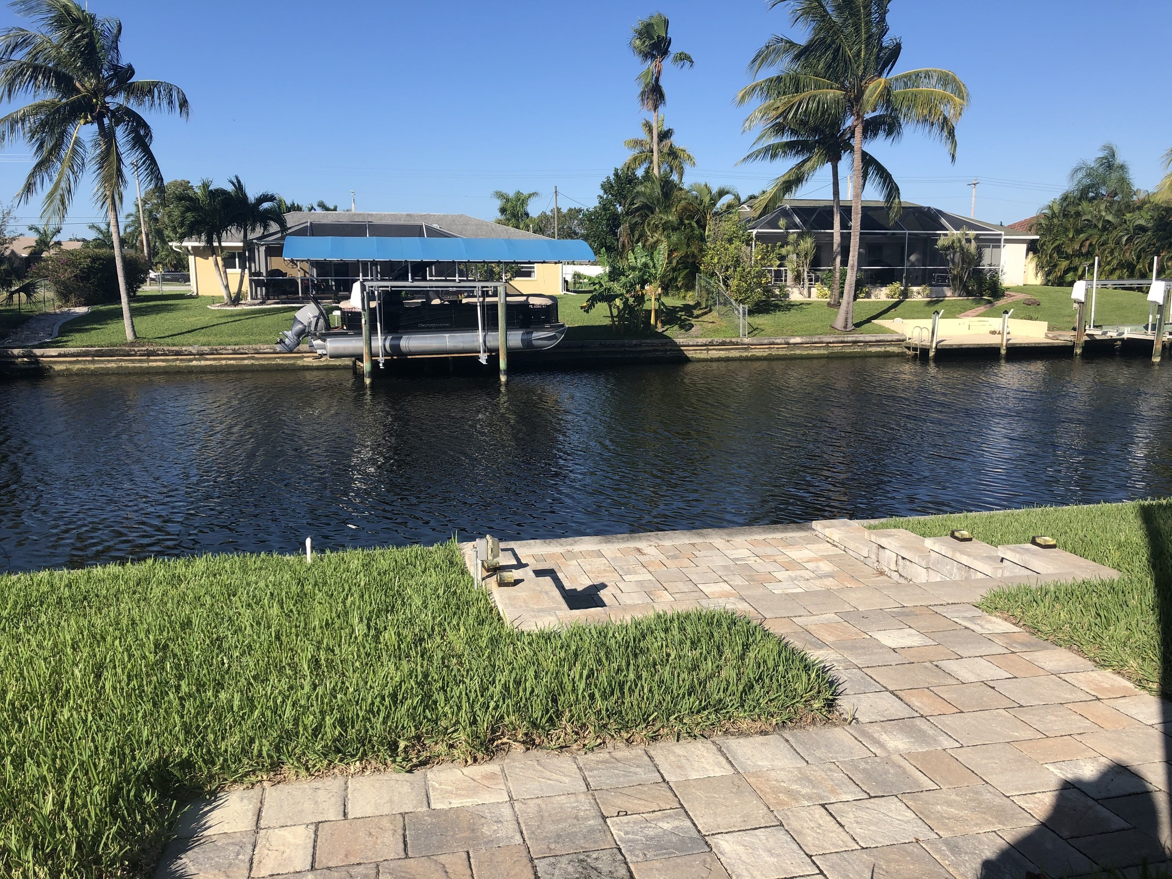 A canal with a boat dock, palm trees, and a paved walkway.