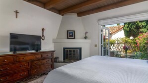 A bedroom with a TV, wooden dresser, fireplace, and a view of a garden. - Enjoy the Beauty of Downtown Santa Barbara Walk Everywhere! (Santa Barbara)