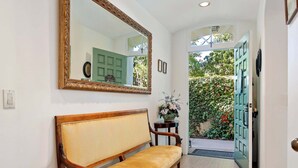 A hallway with a bench, a mirror, a door, and a small table with flowers. - Enjoy the Beauty of Downtown Santa Barbara Walk Everywhere! (Santa Barbara)