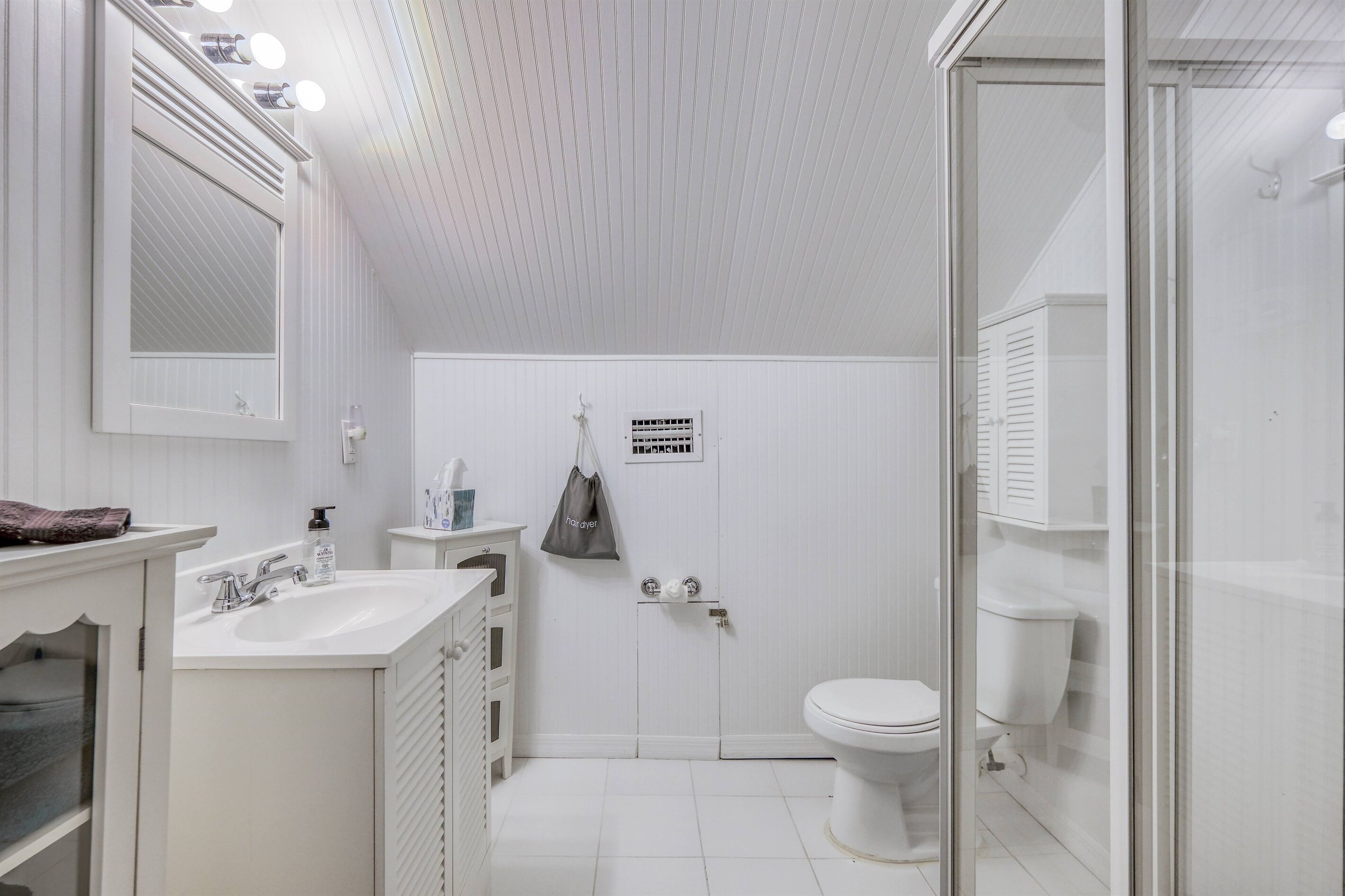 A modern bathroom with a white sink, mirror, and toilet. There is a shower area with a glass door.