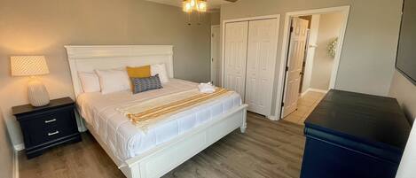 A bedroom with a white bed, a nightstand, a lamp, a ceiling fan, and a wardrobe.