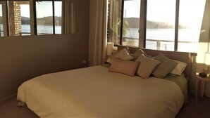 A bedroom with a large bed, a bedside table with a lamp, and a view of a body of water through the window. - Waterfront with private jetty and sunset views. Boat access only. Pet friendly. (little wobby)