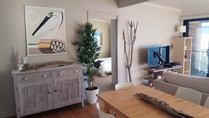 A modern living room with a wooden dining table, a white cabinet, a potted plant, and a television on a stand. - Waterfront with private jetty and sunset views. Boat access only. Pet friendly. (little wobby)