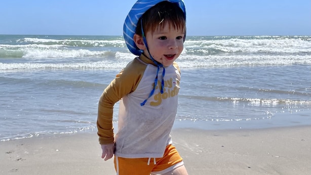 Un bambino su una spiaggia sabbiosa con le onde sullo sfondo.