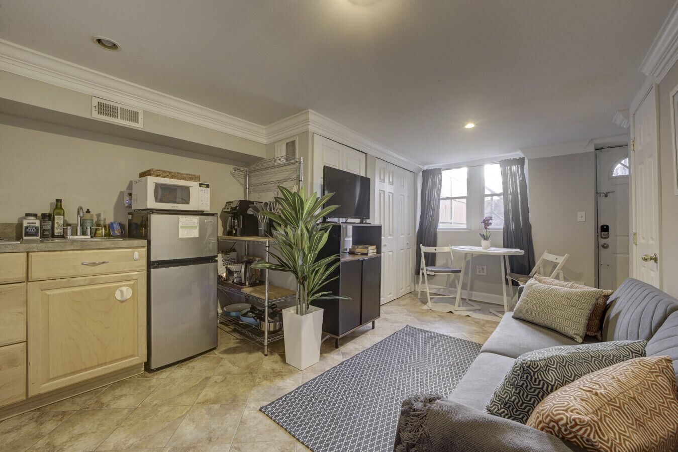 A compact living space with a kitchenette, a dining area, and a seating area with a sofa and cushions.