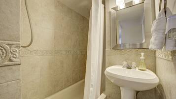 A bathroom with a bathtub, a sink with a soap dispenser, and a mirror above the sink.