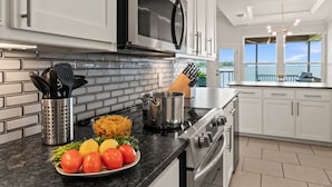 A modern kitchen with white cabinets, a stainless steel microwave, and a large window overlooking a scenic view. - Casa KK | Luxe Lakefront 4BR/3BA w/ Views & Dock (Gun Barrel City)
