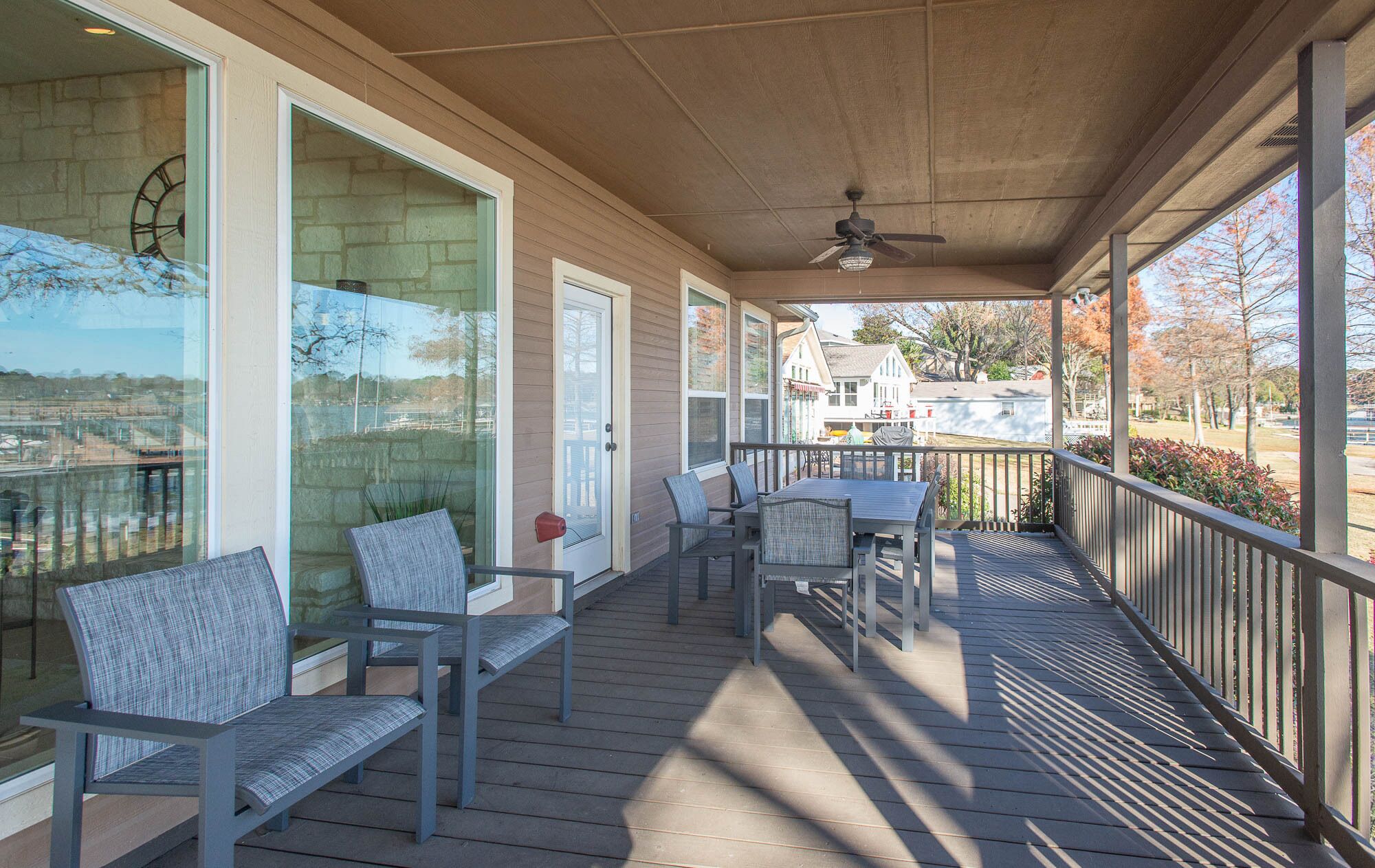 A covered porch with a table and chairs, large windows, and a view of a residential area.