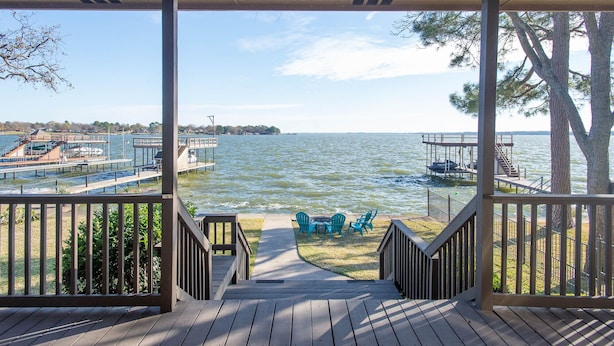 A wooden deck with a view of a lake, a dock, and a boat. - Casa KK | Luxe Lakefront 4BR/3BA w/ Views & Dock (Gun Barrel City)