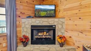 A fireplace with a stone surround, a mounted television above it, and two flower pots on either side. - Smokin Sunrise Cabin (Cosby)