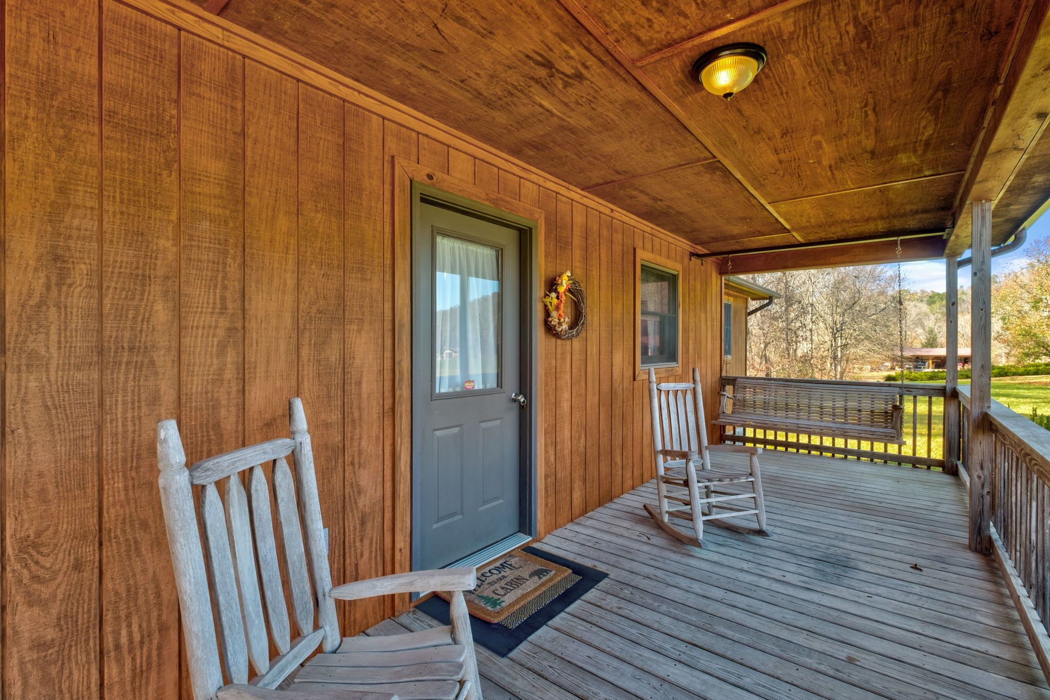 A wooden porch with a door, two rocking chairs, and a bench.