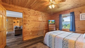 A wooden cabin bedroom with a bed, a TV, and a window with curtains. - Smokin Sunrise Cabin (Cosby)