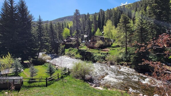 A riverside property with a wooden deck and a view of a mountain forest.