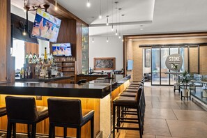 A modern bar area with a long counter, multiple stools, and a television displaying sports.