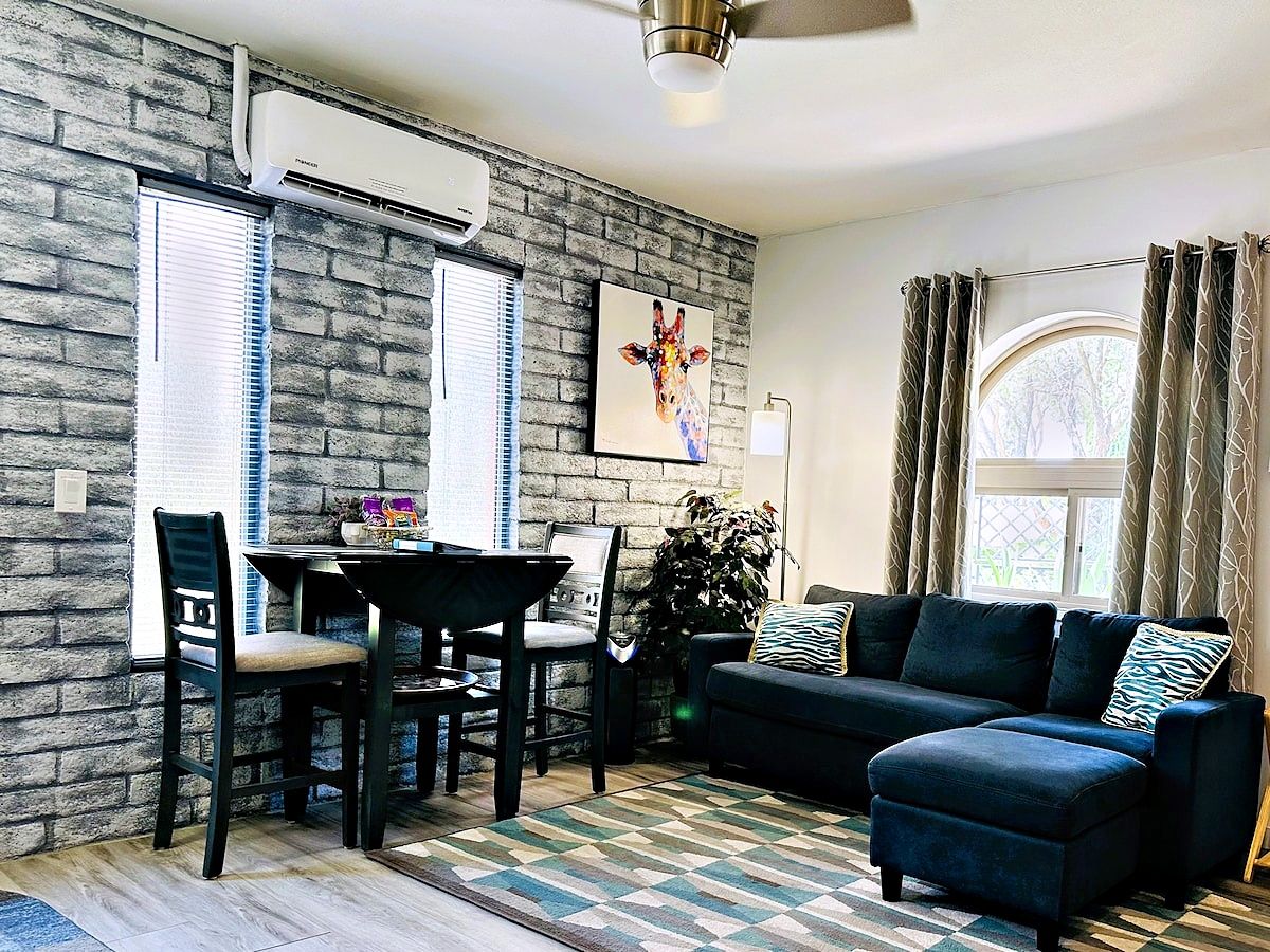 A living room with a brick wall, a dining table with chairs, a sofa, and a ceiling fan.