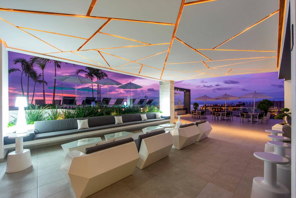 A modern lounge area with a geometric ceiling design, comfortable seating, and a view of the cityscape at dusk.
