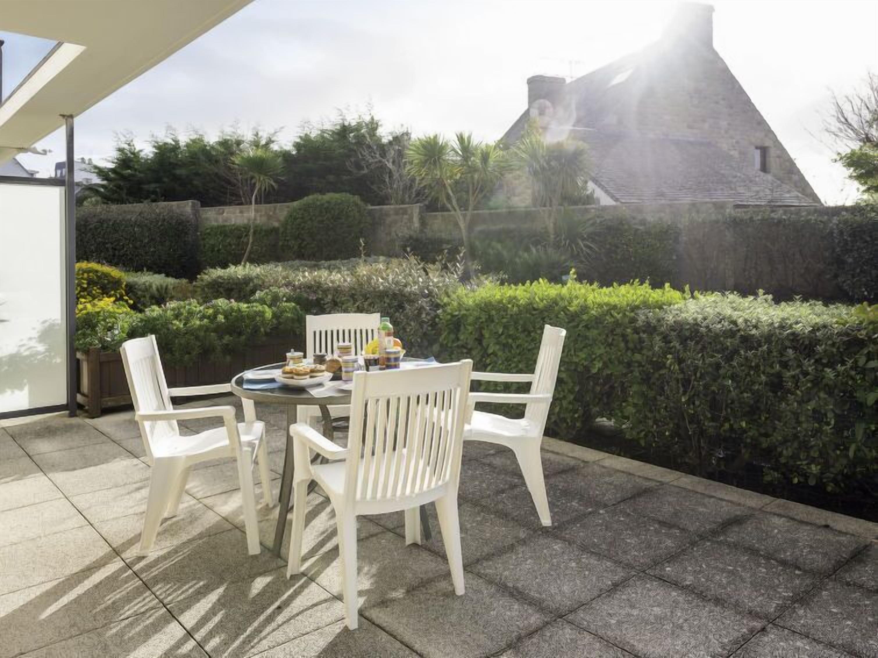 Eine Terrasse mit Tisch und Stühlen, umgeben von Grünpflanzen und einer Steinmauer.