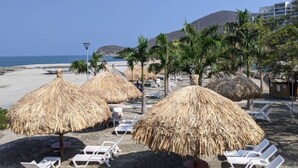 A beach with thatched umbrellas and white lounge chairs, a clear sky, and a mountain in the background. - Beachfront Family Escape | 3BR Samaria Club! (Santa Marta)