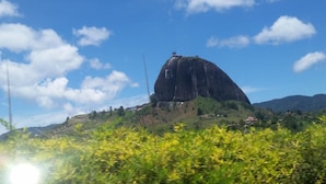 A large, dark-colored building with a flat roof, surrounded by lush greenery and a clear blue sky with scattered clouds. - an anchor for the soul (Guatape)
