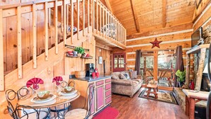 A wooden cabin interior with a dining area, kitchen, and living space. - Just 10 minutes from GSM National Park, 2 BR Log Cabin with Hot Tub & Firepit (Pigeon Forge)