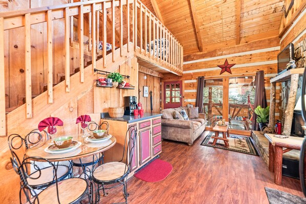 Cozy cabin interior with a warm atmosphere, featuring a wooden staircase, dining area, and a fireplace.