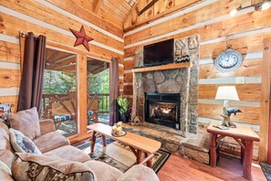 A cozy cabin interior with a stone fireplace, wooden walls, and a comfortable seating area. - Just 10 minutes from GSM National Park, 2 BR Log Cabin with Hot Tub & Firepit (Pigeon Forge)