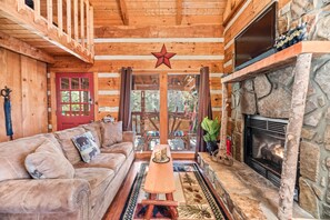 Cozy cabin interior with a rustic aesthetic, featuring a stone fireplace, comfortable sofa, and wooden coffee table.