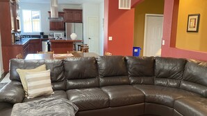 A living room with a dark leather sectional sofa, a dining table, and a kitchen in the background. - Large Independence House for Families & Groups (Independence)