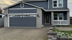 A two-story house with a garage, a front porch, and a brick driveway. - Large Independence House for Families & Groups (Independence)