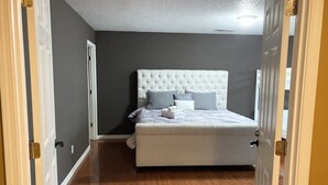 A bedroom with a tufted headboard, a bed with a white mattress and grey bedding, and a wooden floor. - Large Independence House for Families & Groups (Independence)