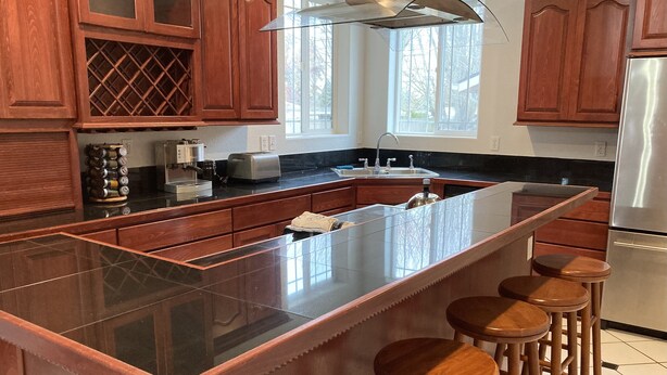 A modern kitchen with a large island, wooden bar stools, stainless steel appliances, and wooden cabinetry. - Large Independence House for Families & Groups (Independence)