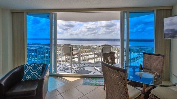 Een balkon met een glazen tafel en stoelen, een bank en uitzicht op de stad en de oceaan.