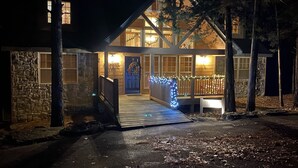 Ein zweistöckiges Haus mit Naturstein-Fassade, einer Holzterrasse und einer Veranda mit Lichterkette.