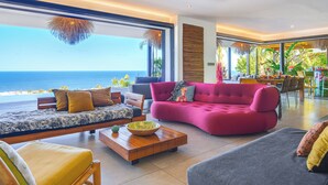 A modern living room with a large sofa, a coffee table, and a view of the ocean. - Villa Coco Palm - Oasis de Luxe 5*- Magnificent Sea View, Private Pool & Jacuzzi (Saint-Pierre)