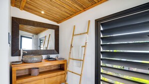 A bathroom with a wooden vanity, a large mirror, and a window with blinds. - Villa Coco Palm - Oasis de Luxe 5*- Magnificent Sea View, Private Pool & Jacuzzi (Saint-Pierre)