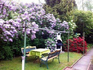 Un jardin avec des fleurs violettes, une mangeoire à oiseaux, un banc et une table.