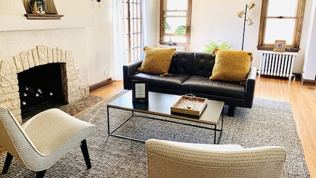 Ein Wohnzimmer mit Kamin, einem schwarzen Ledersofa mit zwei gelben Kissen, einem weißen Sessel und einem Couchtisch.