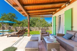 Un espacio de patio cubierto con mobiliario exterior, una piscina y un muro de piedra.
